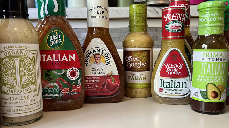 Six+ bottles of italian dressing from different brands including Trader Joe's, Wishbone, Newman's Own, Olive Garden, Ken's Steak House, and Primal Kitchen