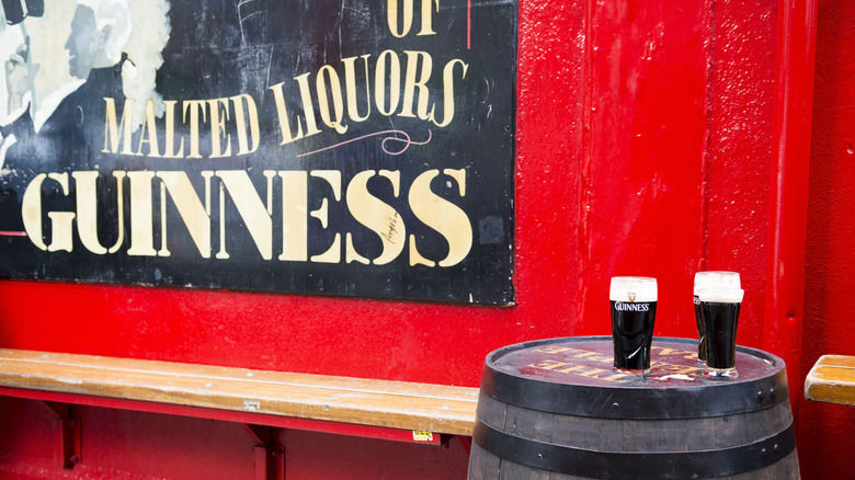 Guinness in pint glasses next to branded metal sign