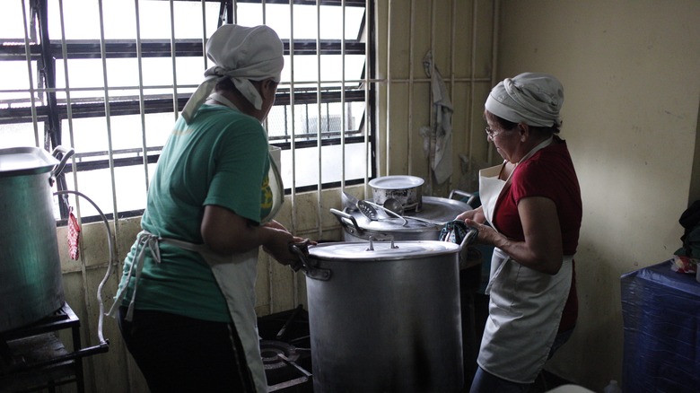 cooks moving a large soup pot in a kitchen