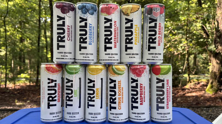 11 flavors of Truly hard seltzer stacked on top of a cooler with woods in the background