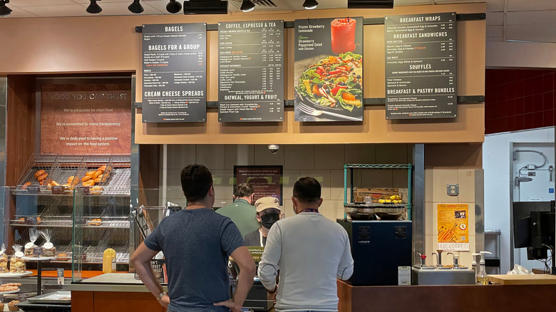 People looking up at a posted Panera restaurant menu behind a counter