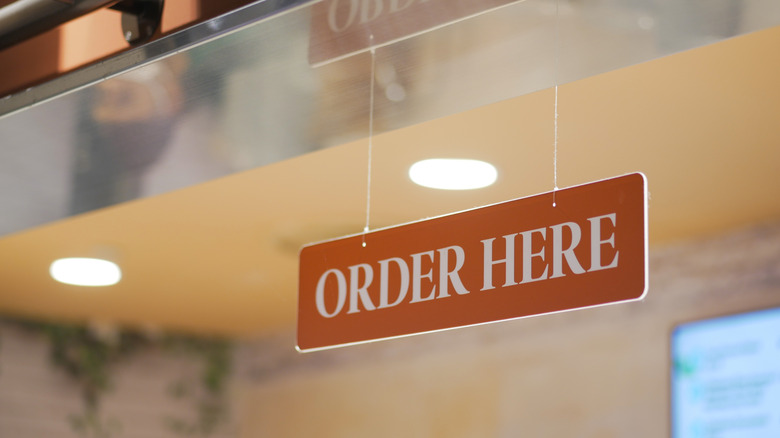 A fast-casual restaurant counter has a sign saying "Order Here"