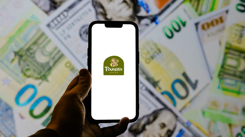 A phone pulling up the Panera app is held in front of various currency