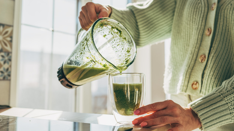 Hand pouring a drink from a blender jug into a glass