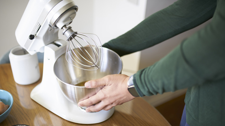 White stand mixer with silver bowl being held by hands