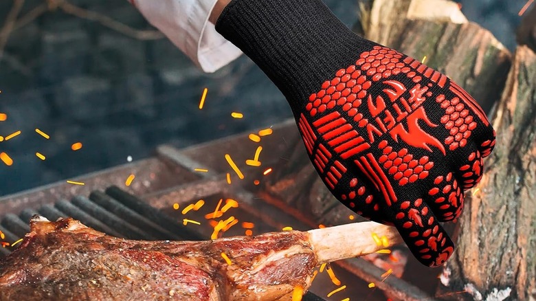 Someone wearing a Fitfiv﻿ glove grabs meat straight off the grill by the bone.