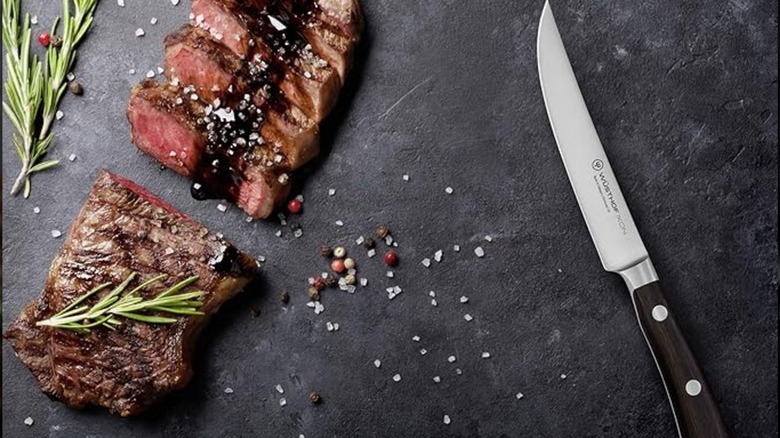 A steak knife on a wooden table next to sliced steak.