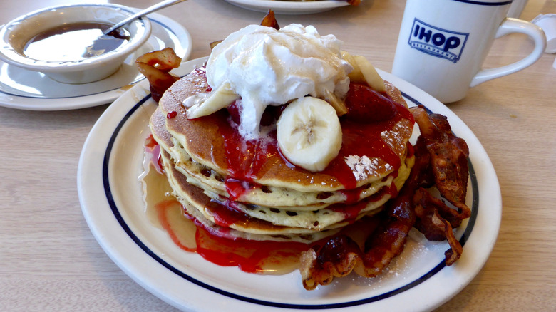 A stack of IHOP pancakes topped with strawberries, bananas, and whipped cream.