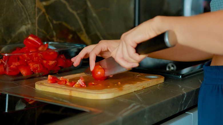 A professional cook slices cherry tomatoes with the tip of her knife