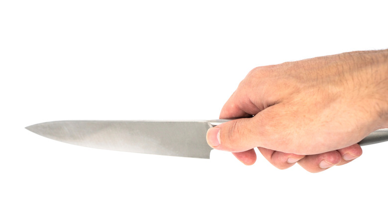 Hand holds a large kitchen knife with a pinch grip, in front of a white background