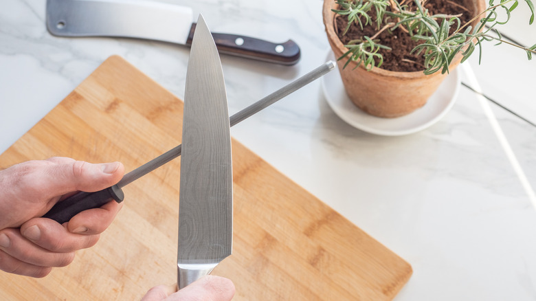 Closeup of hands honing a chef's knife with a honing rod over a cutting board