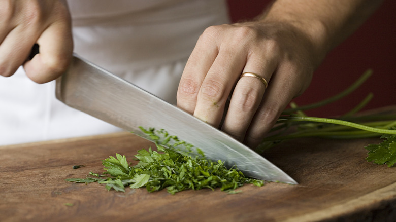 Man in chef whites chopping parsley with a chef's knife