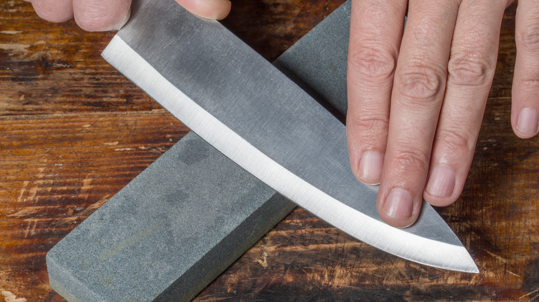 Closeup of hands sharpening a chef's knife against a whetstone