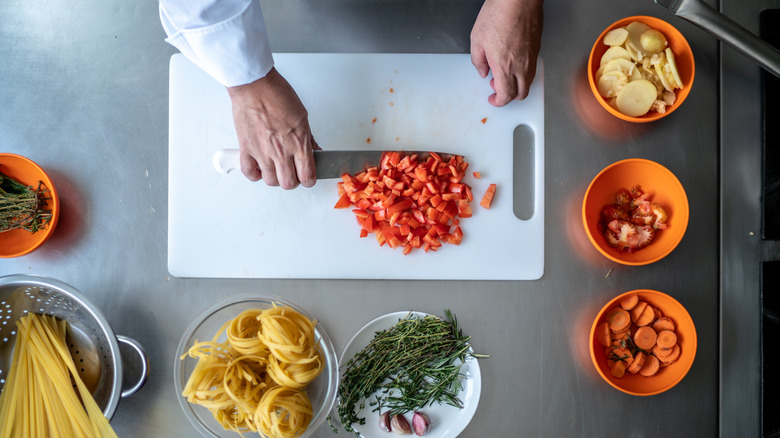 Close up of hands using a knife blade to scrape chopped tomatoes off a cutting board