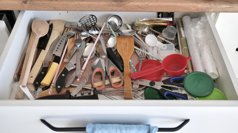 Knives and many other varied utensils sit cluttered in a junk drawer