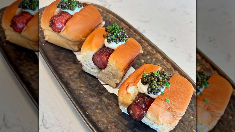 a hot dog has been sliced into thirds and each is topped with creme fraiche and caviar