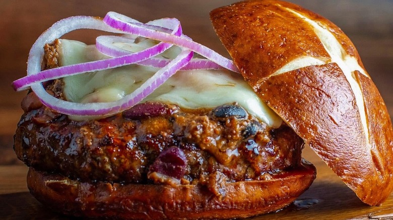 close up of burger with chili, cheese, and onions on a pretzel bun