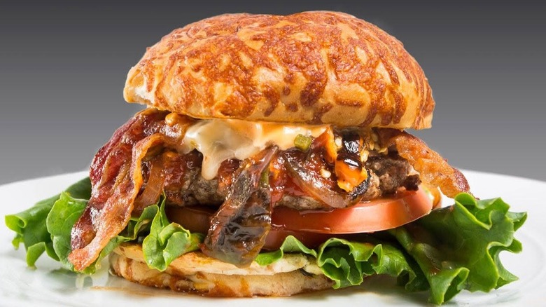 close up of a burger on a cheesy bun with bacon, caramelized onions, cheese, lettuce, and tomato