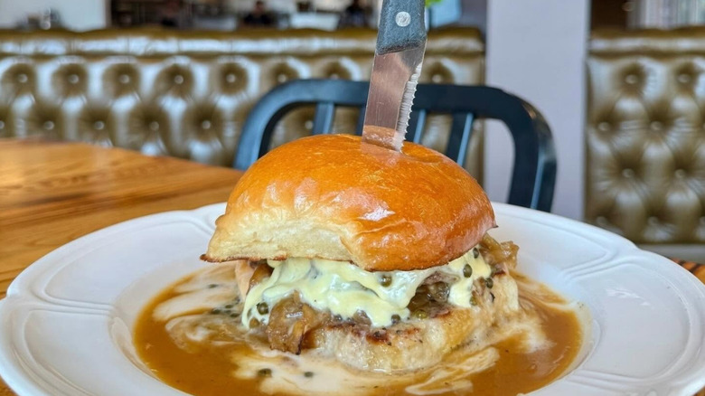 a cheeseburger surrounded by sauce on a plate with a knife stuck in the center