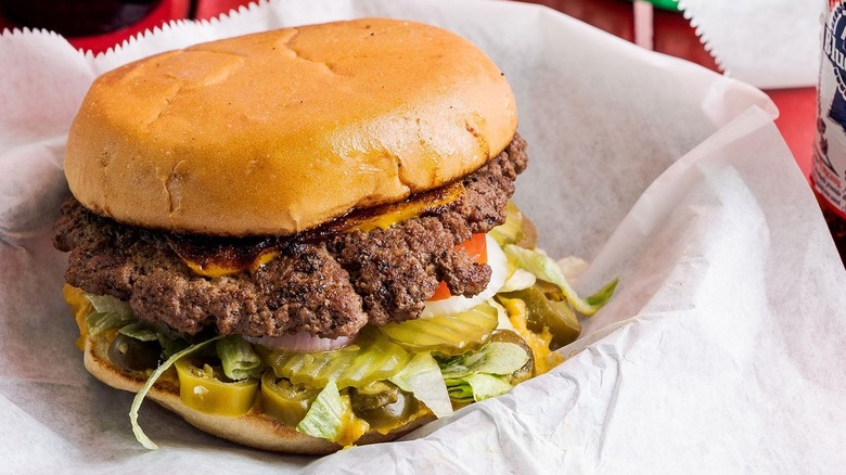 close up of a burger in a paper basket with pickles, jalapenos, and cheese