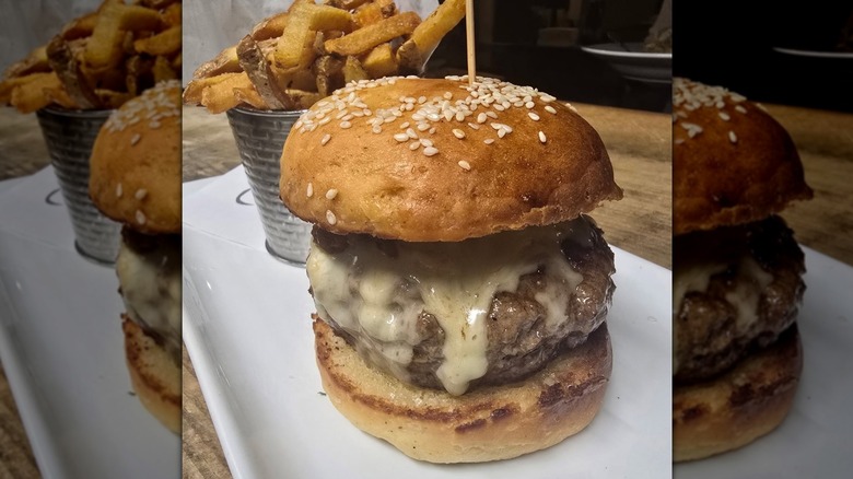 a large burger with melted cheese next to a bucket of fries on a plate