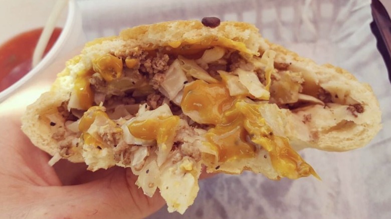 closeup of a krautburger cut open with beef and cabbage filling next to a pickle