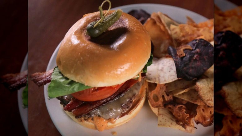 top down shot of a burger on a plate with a cornichon on top next to chips