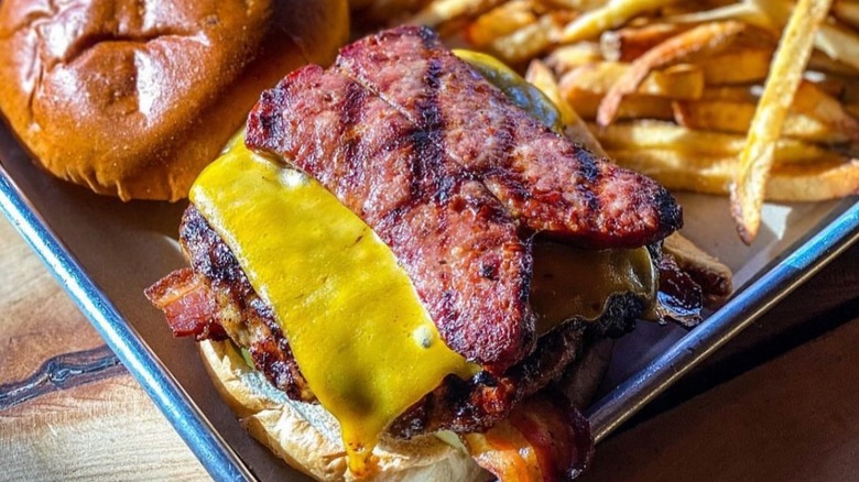 an open faced burger with bacon, cheese, and sausage next to fries