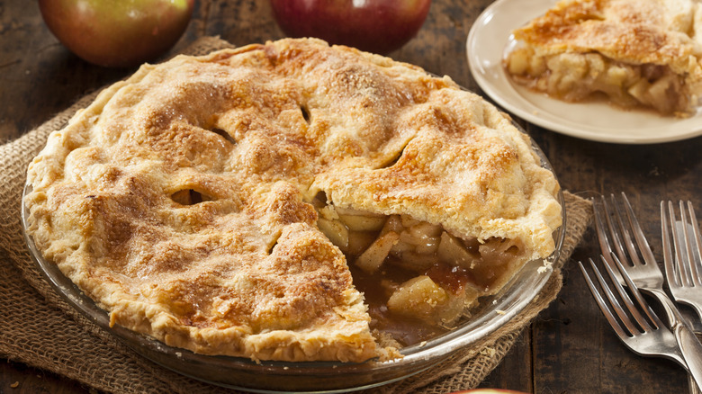 A homemade apple pie with a slice cut out sits on a table.
