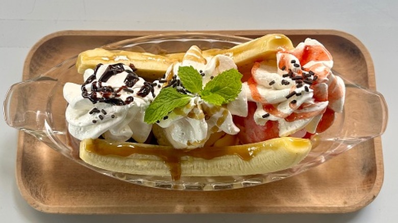 A banana split sundae is in a dish on a plate.