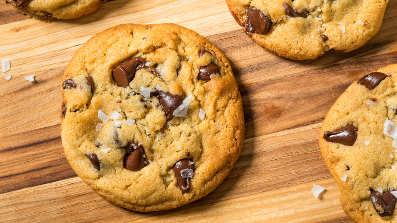 A homemade chocolate chip cookie sits on a wooden board.