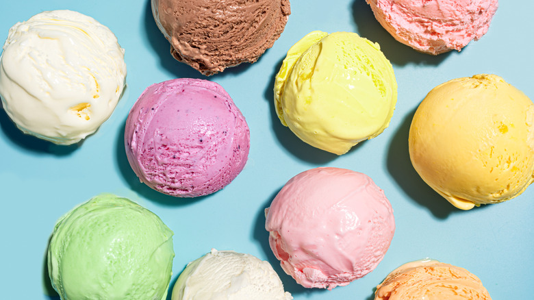 assorted scoops of colorful ice cream sit on a teal background.