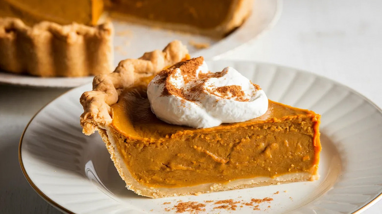 A slice of pumpkin pie sits on a plate with a dollop of whipped cream on top.