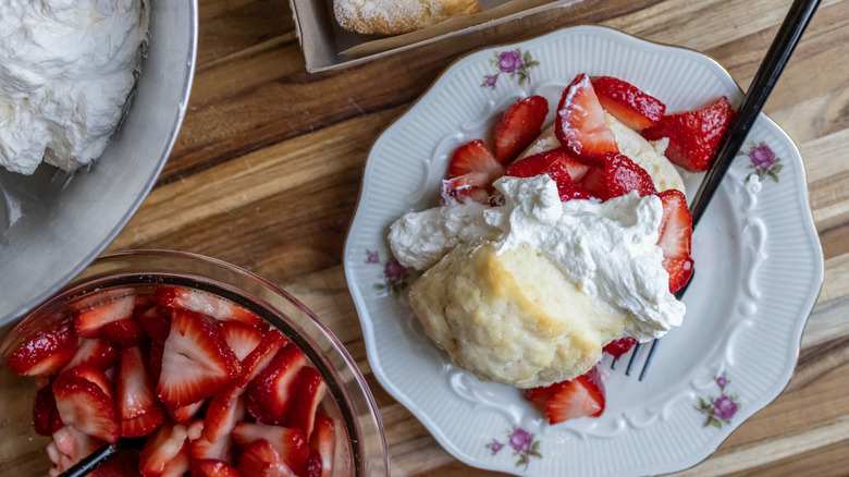a plate of strawberry shortcake surrounded by strawberries and whipped cream is on a table.