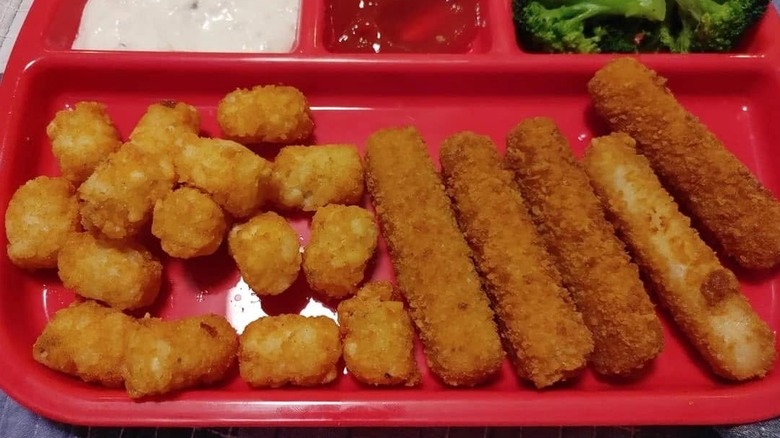 a red plastic lunch tray with tater tots and fish sticks, dipping sauces, and broccoli