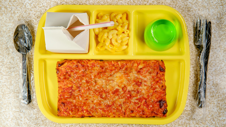 a yellow plastic lunch tray with a carton of milk, mac and cheese, green gelatin, and a rectangle pizza