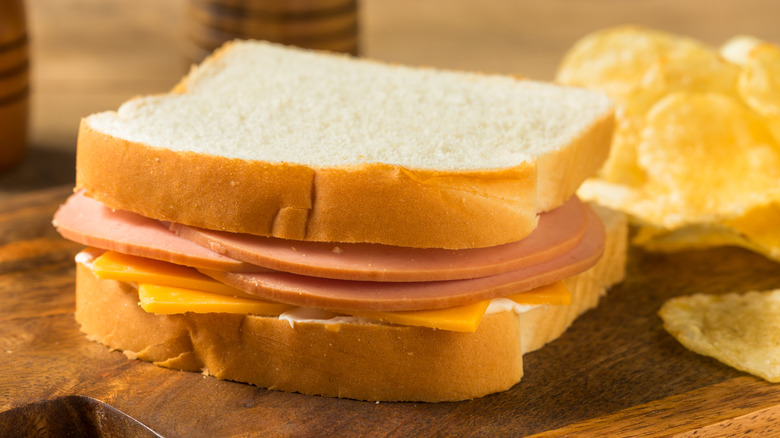 white bread sandwich with bologna and american cheese beside potato chips