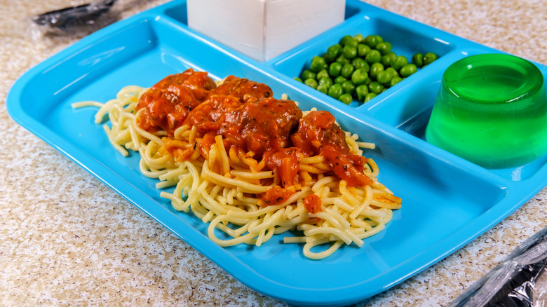 a blue plastic lunch tray with spaghetti and meat sauce, green gelatin, peas, and milk.