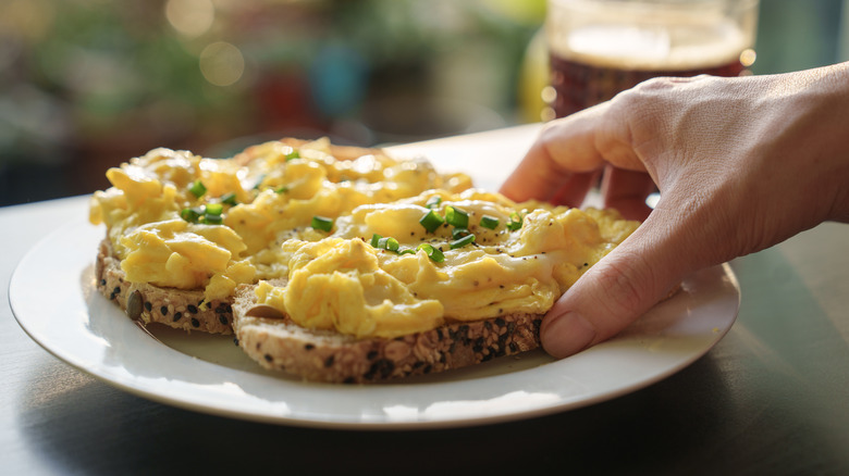 Hand grabbing toast topped with scrambled eggs