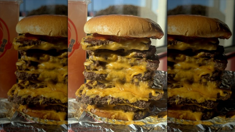 9-patty T-Rex Burger from Wendy's in front of a window and Wendy's plastic cup