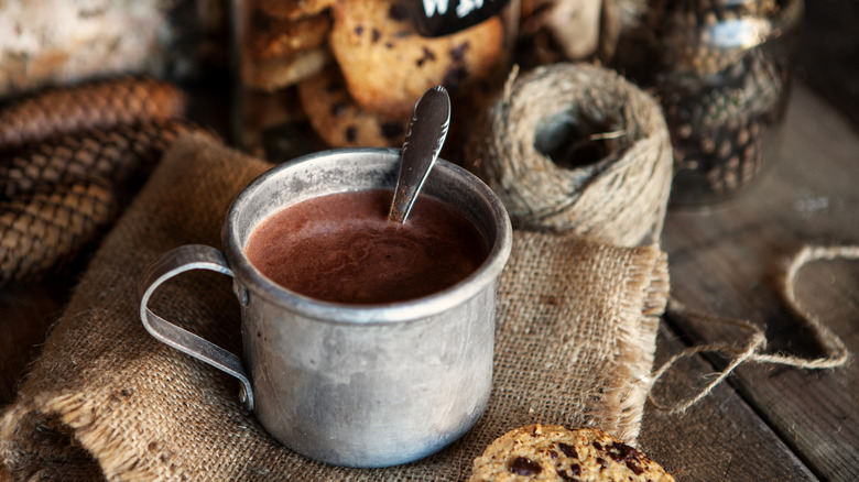 Hot chocolate in a steel mug with a spoon on a burlap sack.