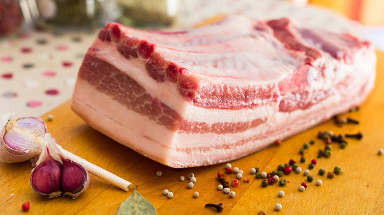 A cut of pork belly on a cutting board with garlic and peppercorns