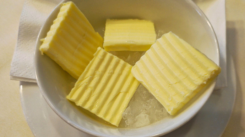 Pats of textured butter sit in a bowl of ice.