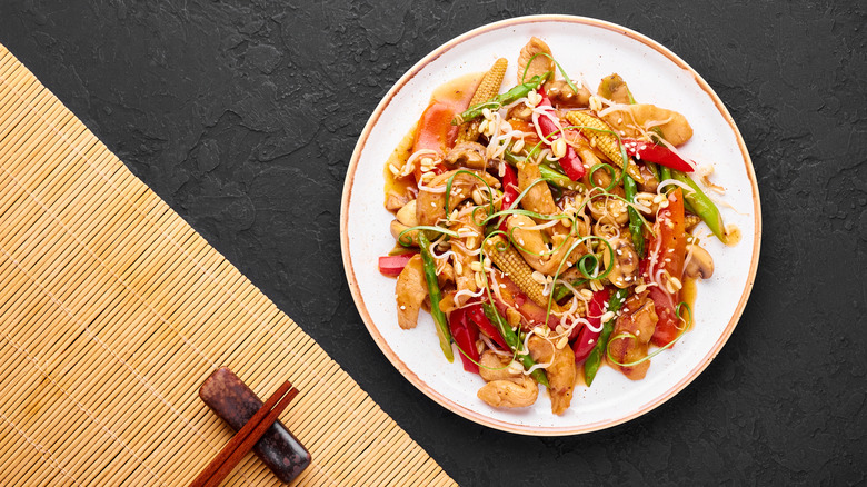 A plate of chicken chop suey sits next to chopsticks on a table.