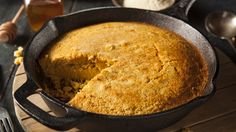 Cornbread is in a cast iron skillet with a single slice removed.