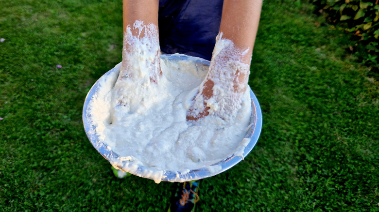 A person is mixing flour and water together outside.