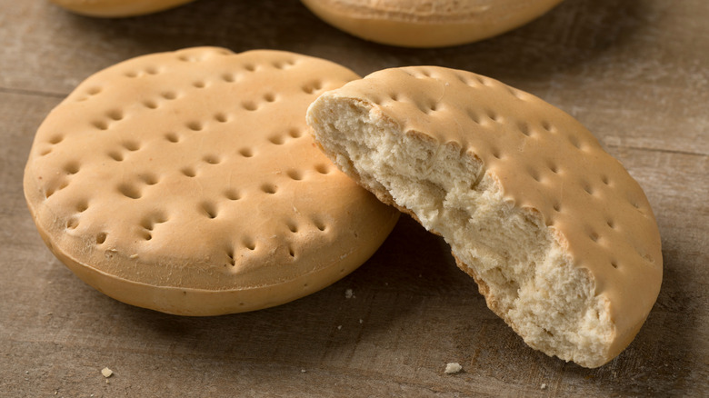 Two pieces of hardtack, one half-gone, sit on a wooden table.