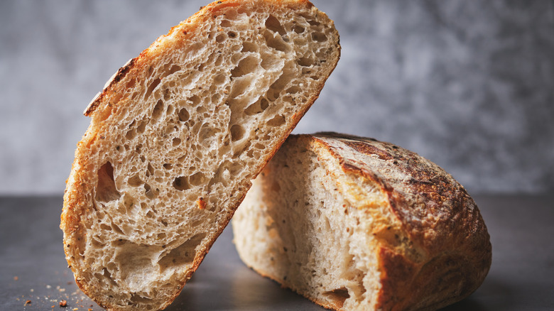 A loaf of sourdough is cut in half, with one half leaning on the other in front of a gray background.