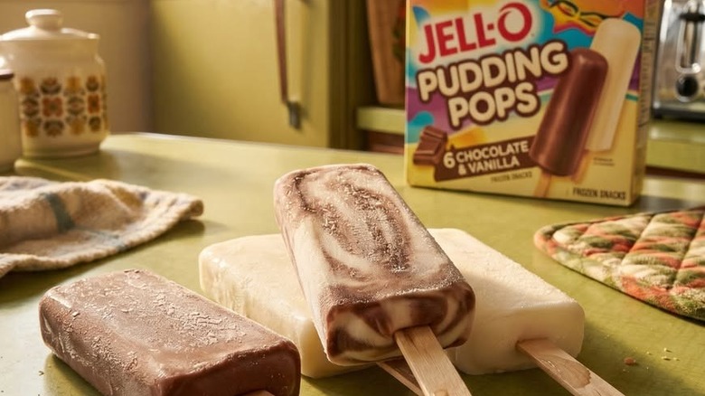 Chocolate, vanilla, and swirls pudding pops lie on a vintage-looking kitchen counter with the Jell-O Pudding Pops box in the background