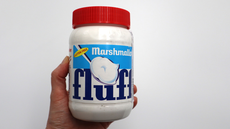 A hand holding a jar of Marshmallow Fluff